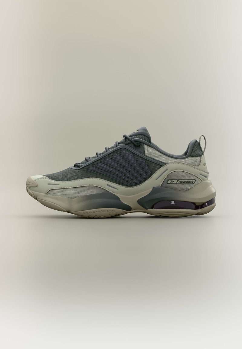 Szary i beżowy sportowy but Reebok z siateczkową cholewką, amortyzowaną podeszwą i pętelką do łatwego zakładania na neutralnym tle, pokazany w profilu bocznym.