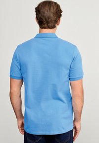 Koszulka polo w jasnoniebieskim kolorze, wykonana z bawełny, z klasycznym kołnierzykiem i krótkimi rękawami. Gładka struktura z zaokrąglonym dołem, pokazany widok z tyłu.
