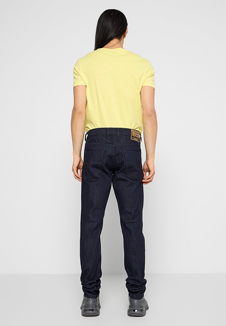 T-shirt giallo a collo rotondo, jeans blu scuro, vestibilità casual. Denim texturizzato, cinque tasche, cuciture visibili, scarpe con suola di gomma.