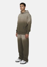 Olijfgroen pullover hoodie met een verloopkleur, voorzak, losse fit. Gecombineerd met bijpassende joggers, zachte textuur, afgewerkt met witte sneakers.