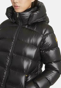 Zwarte pufferjas met een glanzende, doorgestikte textuur; voorzien van een hoge kraag, volledige rits en een logopatch op de linkermouw.