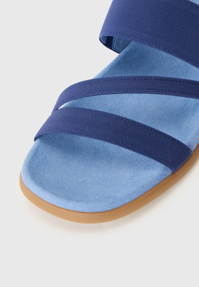 Niebieska sandał z miękką zamszową cholewką i granatowymi materiałowymi paskami. Posiada okrągły czubek i jasnobrązową gumową podeszwę dla lepszej przyczepności.