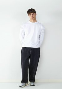 Biała koszula z długim rękawem, ciemne luźne dżinsy i szare sneakersy. Minimalistyczny design, regularny krój, z prostą nogawką i kontrastowym przeszyciem.