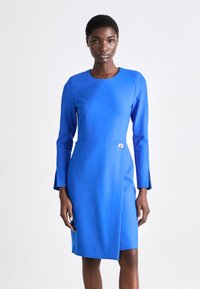 Μπλε μακρύ φόρεμα με μακριά μανίκια, φτιαγμένο από λείο ύφασμα, που διαθέτει στρογγυλή λαιμόκοψη και διακοσμητικό κουμπί στη μέση. Απλός, δομημένος σχεδιασμός.