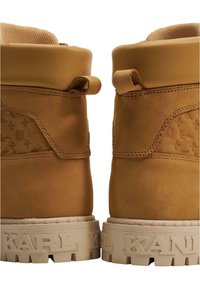 Brune lær ankle boots med et teksturert design og forsterkede snøringer, med en beige gummisåle som har "KARL" preget på siden.