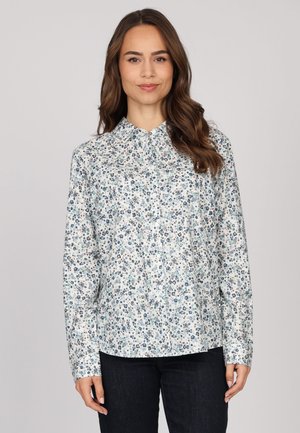 Chemise à manches longues boutonnée en tissu blanc avec un motif floral coloré comportant des accents bleus, verts et roses. Texture lisse, col pointu.