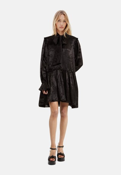 Schwarzes Satin-Kleid mit langen Ä sleeves, hohem Kragen und Schleifen-Detail, mit geraffter Taille und ausgestelltem Saum. Texturiertes Muster im gesamten Kleid.