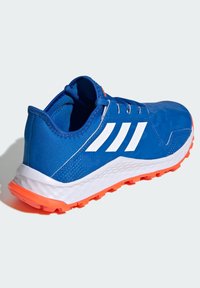 Niebieski but sportowy z białymi paskami, z syntetyczną cholewką, teksturowaną pomarańczową podeszwą oraz białą śródpodeszwą. Zaprojektowany dla lepszej przyczepności.