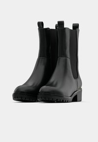 Crne kožne gležnjače s elastičnim bočnim panelima, zaobljenim prstima i teksturiranom gumenenom potplatu. Imaju uvučene ručke za lakše obuvanje i složen petu.