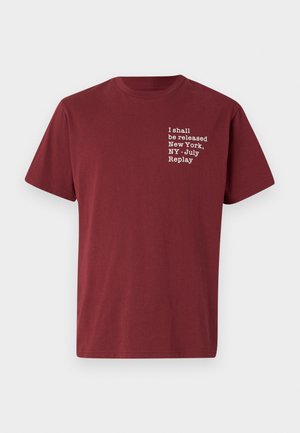 Bordo pamučna majica s kratkim rukavima i okruglim izrezom, s bijelim natpisom: "Bit ću oslobođen New York, NY - Srpanj Replay" na prsima.