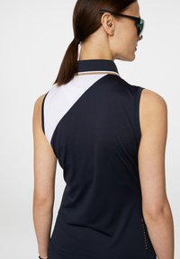 Ärmlös polo i marinblå med vit detalj; har en hög krage, sportig passform, texturerad tyg och subtil logotypdetalj.