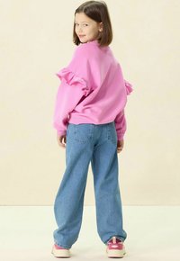 Un sweatshirt rose avec des manches volantes, associé à un jean large bleu clair. La tenue est complétée par des baskets roses et blanches.