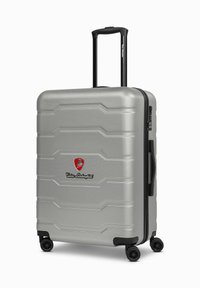 Maleta rígida plateada con superficie texturizada, cremallera negra y logo. Cuenta con un mango telescópico y cuatro ruedas giratorias para mayor movilidad.