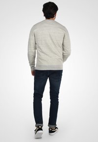 Suéter texturizado de color gris claro con cuello redondo, combinado con jeans azul oscuro y zapatillas negras con suelas blancas y detalles claros.
