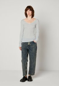 Ljust grå långärmad topp med v-ringad design och figurnära siluett, i kombination med högmidjade blå jeans och svarta slip-on skor.