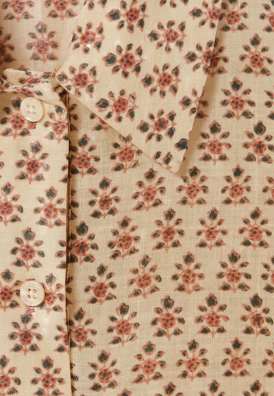 Tela con un estampado floral que presenta pequeñas flores rojas y verdes sobre un fondo beige. Cuenta con un cierre de botones y bordes de cuello nítidos.