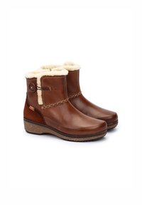 Botas de cuero marrón hasta el tobillo con forro de piel sintética, acentos texturizados y un detalle decorativo de cadena. Suela de goma gruesa para mayor soporte.