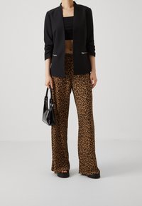 Černé sako s dlouhými rukávy, otevřené vpředu, doplněné širokými kalhotami s leopardím vzorem v hnědé a černé barvě. Černá kabelka outfit doplňuje.