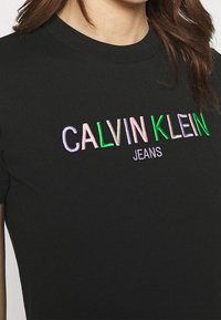 Černé bavlněné tričko s vyšívaným nápisem "CALVIN KLEIN" v mnoha barvách a "JEANS" v bílé, s klasickým kulatým výstřihem.