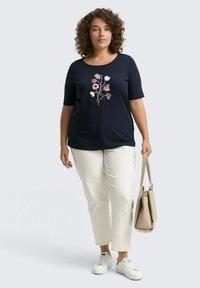 T-shirt marine à manches courtes avec broderie florale rose et blanche, associé à un pantalon crème et un sac à main beige. Baskets blanches.