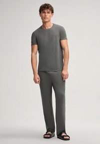 Grijze t-shirt en bijpassende broek van zacht materiaal, met een ronde halslijn en een slim fit. Platte schoenen maken de look compleet.