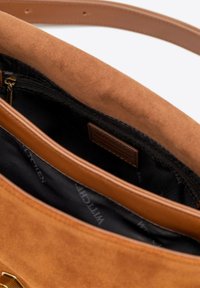 Bruine suède handtas met een zachte textuur, een ritsvak en een zwarte binnenvoering met een merklogo.