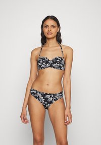 Juodas bikini komplektas, kuriame yra be rankovių viršus su baltais gėlių raštais ir atitinkančios žemai kelnaitės, pagamintos iš lygios, elastingos medžiagos.