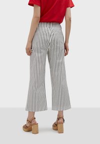Biele široké nohavice s čiernymi vertikálnymi pruhmi, s vysokým pásom a zadnými vreckami, doplnené o hnedé sandále na podpätku.