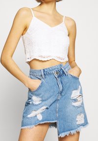 Weißes Spitzen-Crop-Top mit dünnen Trägern, kombiniert mit einem hellblauen Jeans-Minirock, der zerstörte Risse und einen ausgefransten Saum aufweist.