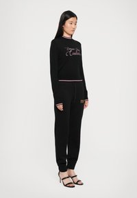Svart ribbet genser med rosa broderi og matchende mansjetter, parret med svarte joggebukser med stilige detaljer og tettsittende ankelmansjetter.