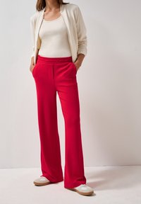 Rode joggerbroek met een textuurpatroon, elastische tailleband, zijzakken, gecombineerd met een crème getailleerde top en lichtgekleurde schoenen.