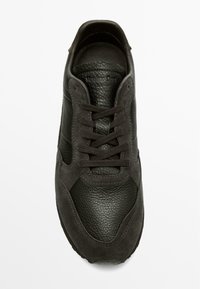 Černá kožená teniska s semišovými boky a kulatou špičkou. Šněrovadla jsou hnědá; vnitřek má texturovanou koženou podšívku. Kožené značení na jazyku.