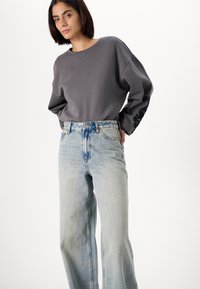 Sweatshirt gris avec broderie noire sur la manche, associé à un jean large taille haute bleu clair. Tissu doux, coupe décontractée.