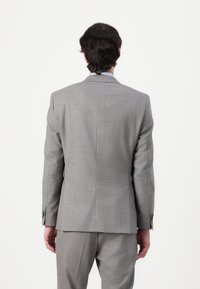 Completo grigio con tessuto testurizzato, design su misura, con apertura singola e polsini abbottonati. Vista posteriore che mostra una forma strutturata e linee pulite.