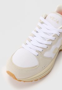 White mesh and beige suede sneaker with flat white laces, a curved shape, rubber sole, and subtle branded detail on the tongue.