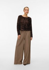 Tumši ķiršsarkana blūze ar spīdīgu spīguļu rotājumu un garām piedurknēm, kopā ar augsta jostasvietas plašām bēšām biksēm un smailām brūnām kurpēm.