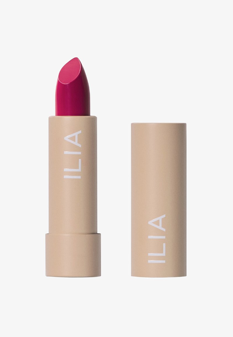 El lápiz labial ILIA en un tubo beige claro presenta un bullet magenta brillante y vibrante. La etiqueta dice "ILIA" en texto blanco, con un acabado mate suave.