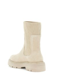 Beige ruskind ankelstøvle med ribbet tekstil skaft, flad gummisål og synlig syning. Enkel og funktionel design.