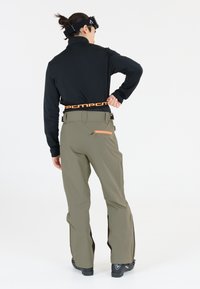 Schwarzes Langarm-Oberteil kombiniert mit olivgrünen Skihosen, die über einen orangefarbenen Gürtel und Reißverschlusstaschen verfügen, entworfen für Aktivitäten im Freien.