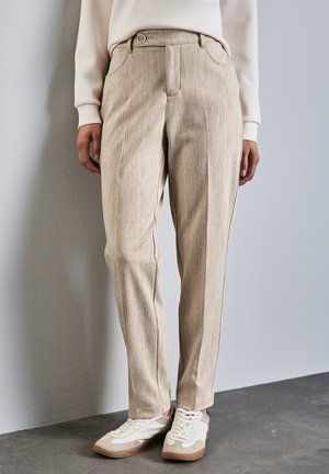 Pantalons rayés beige clair avec une fermeture à bouton à l'avant, des poches latérales et une coupe slim, associés à des baskets blanches et beige.