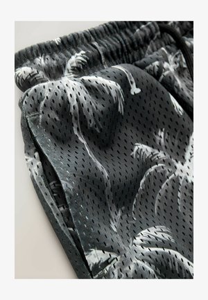 Černé šortky vyrobené z lehké perforované látky s bílým vzorem palmových stromů a elastickým pasem se šňůrkou.