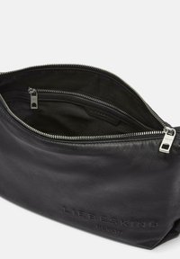 Borsa in pelle nera con texture liscia, dotata di una zip argentata e logo impresso sul davanti. L'interno è rivestito in tessuto nero.