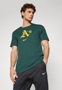 Zelené bavlnené tričko s veľkým žltým logom "A's" a malým bielym logom Nike. Okrúhly výstrih, krátke rukávy, voľný strih.