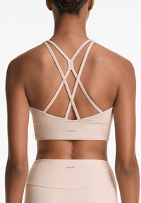 Beige sportbh met een gladde textuur, voorzien van kruislings gespen op de rug en een subtiele OYSHO-logo op de onderste band.
