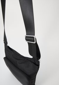 Borsa a spalla nera realizzata in tessuto liscio, dotata di una tracolla staccabile, una tasca con zip e un design elegante e minimalista.