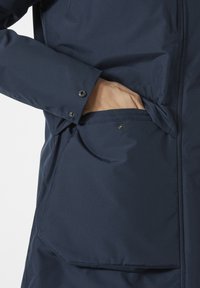 Navy blue jacket featuring a secure side pocket, smooth texture, and snap button closure on the cuff, displaying a practical design.