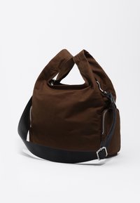 Brązowa torba materiałowa z dwiema górnymi rączkami, odpinanym czarnym paskiem oraz srebrnymi zamkami po bokach do przechowywania. Miękka, zarysowana forma.