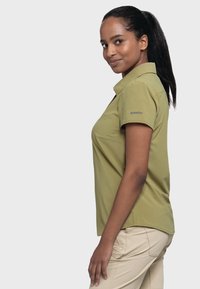 Olive green polo shirt with short sleeves, collar, and logo on the left arm. Smooth texture, tailored fit, paired with light khaki pants.