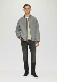 Szara kurtka bomberka z prążkowanymi mankietami, suwakiem z przodu i bocznymi kieszeniami, w połączeniu z ciemnymi dżinsami i czarnymi sneakrsami, na jednolitym tle.
