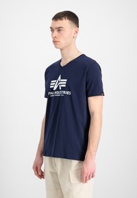 Bordo modri bombažni T-shirt z V-izrezom in belim logotipom. Kratki rokavi z diskretnim logotipom na levi roki. Gladka tekstura.